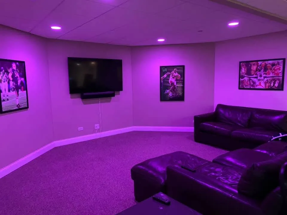 Finished recreation room with wall art, seating, and purple accent lighting